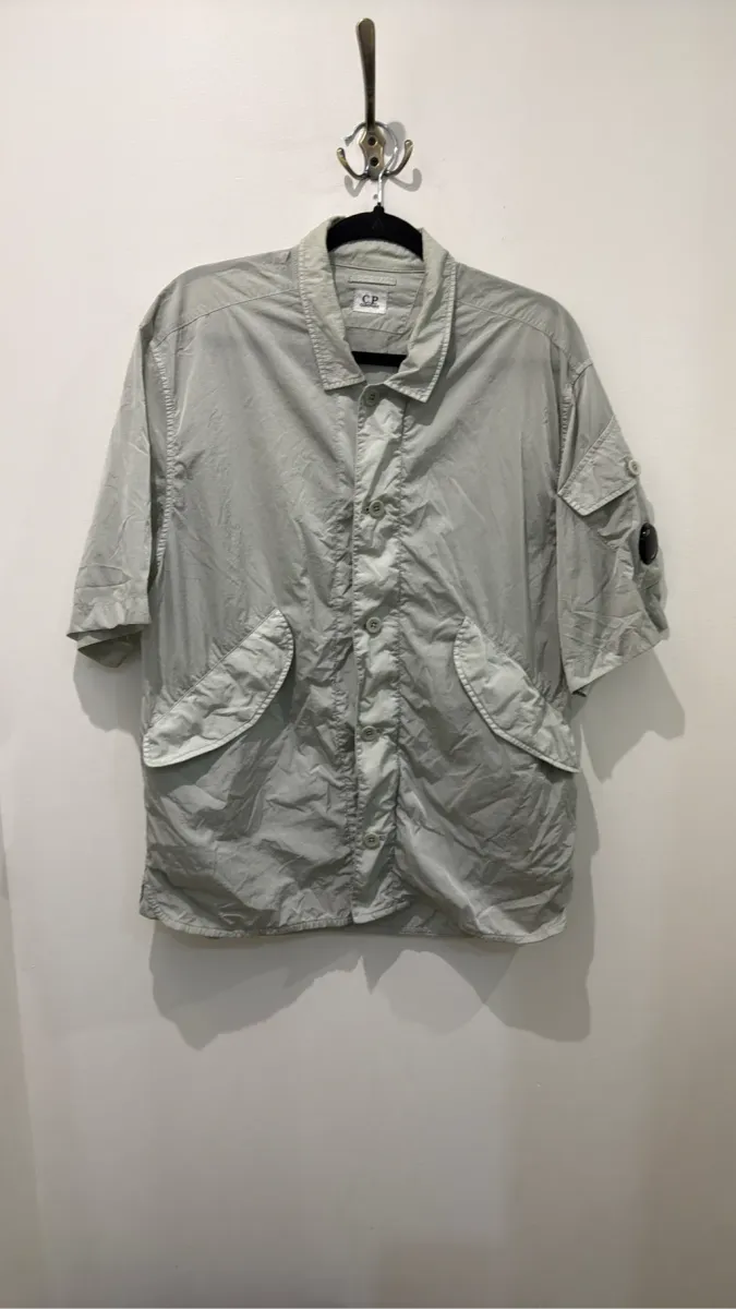 Chemise-veste à manches courtes C.P. Company en nylon recyclé Chrome-R, de couleur gris clair, avec un patch logo sur la manche.