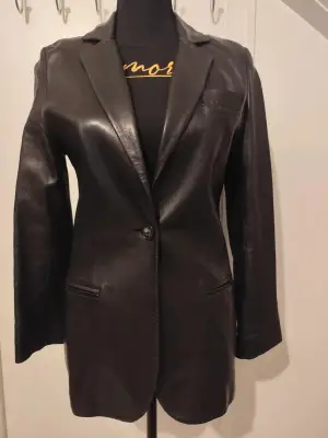 Belle veste en cuir d'agneau plongé, souple et doux, de fabrication française 
Col tailleur, forme légèrement cintrée 
Entièrement doublée
Fermeture par un bouton 
Une petite poche poitrine et deux fausses poches passepoilées devant 
Longueur 70cm, aisselle à aisselle 43cm, tour de taille à plat 37cm
Très bon état, beau cuir sans défaut