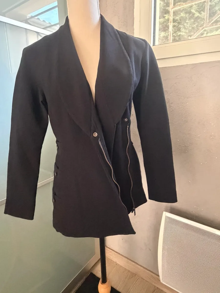 ✨ Une pièce vintage d'exception au style couture et affirmé ! Superbe veste de tailleur / blazer vintage noir de la marque créateur Tony La Marca France, coupe travaillée et très élégante. ✨ Détails & Coupe : Col châle croisé à l'avant, fermeture par bouton, détails de petits boutons décoratifs structurant le côté de la taille. Tissu côtelé / strié de très belle tenue. 📐 Dimensions & Taille : Largeur aisselle à aisselle : 47 cm (convient à un 38 - M). 🧵 Qualité : Belle confection française vintage, pièce originale et structurée. 8