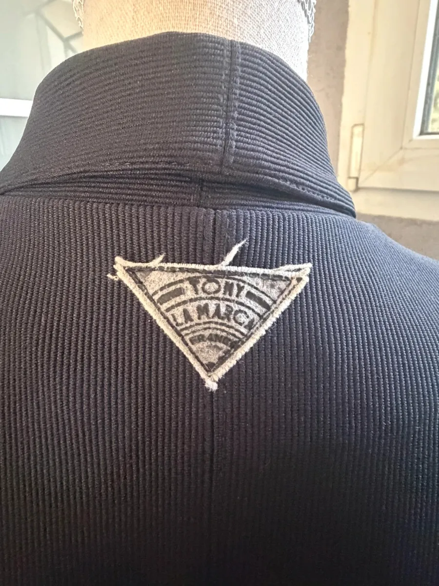 ✨ Une pièce vintage d'exception au style couture et affirmé ! Superbe veste de tailleur / blazer vintage noir de la marque créateur Tony La Marca France, coupe travaillée et très élégante. ✨ Détails & Coupe : Col châle croisé à l'avant, fermeture par bouton, détails de petits boutons décoratifs structurant le côté de la taille. Tissu côtelé / strié de très belle tenue. 📐 Dimensions & Taille : Largeur aisselle à aisselle : 47 cm (convient à un 38 - M). 🧵 Qualité : Belle confection française vintage, pièce originale et structurée. 4