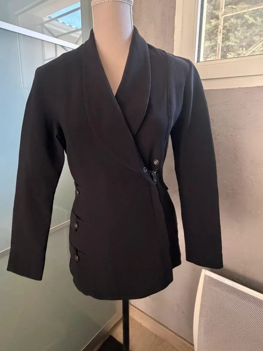 ✨ Une pièce vintage d'exception au style couture et affirmé ! Superbe veste de tailleur / blazer vintage noir de la marque créateur Tony La Marca France, coupe travaillée et très élégante. ✨ Détails & Coupe : Col châle croisé à l'avant, fermeture par bouton, détails de petits boutons décoratifs structurant le côté de la taille. Tissu côtelé / strié de très belle tenue. 📐 Dimensions & Taille : Largeur aisselle à aisselle : 47 cm (convient à un 38 - M). 🧵 Qualité : Belle confection française vintage, pièce originale et structurée. 6