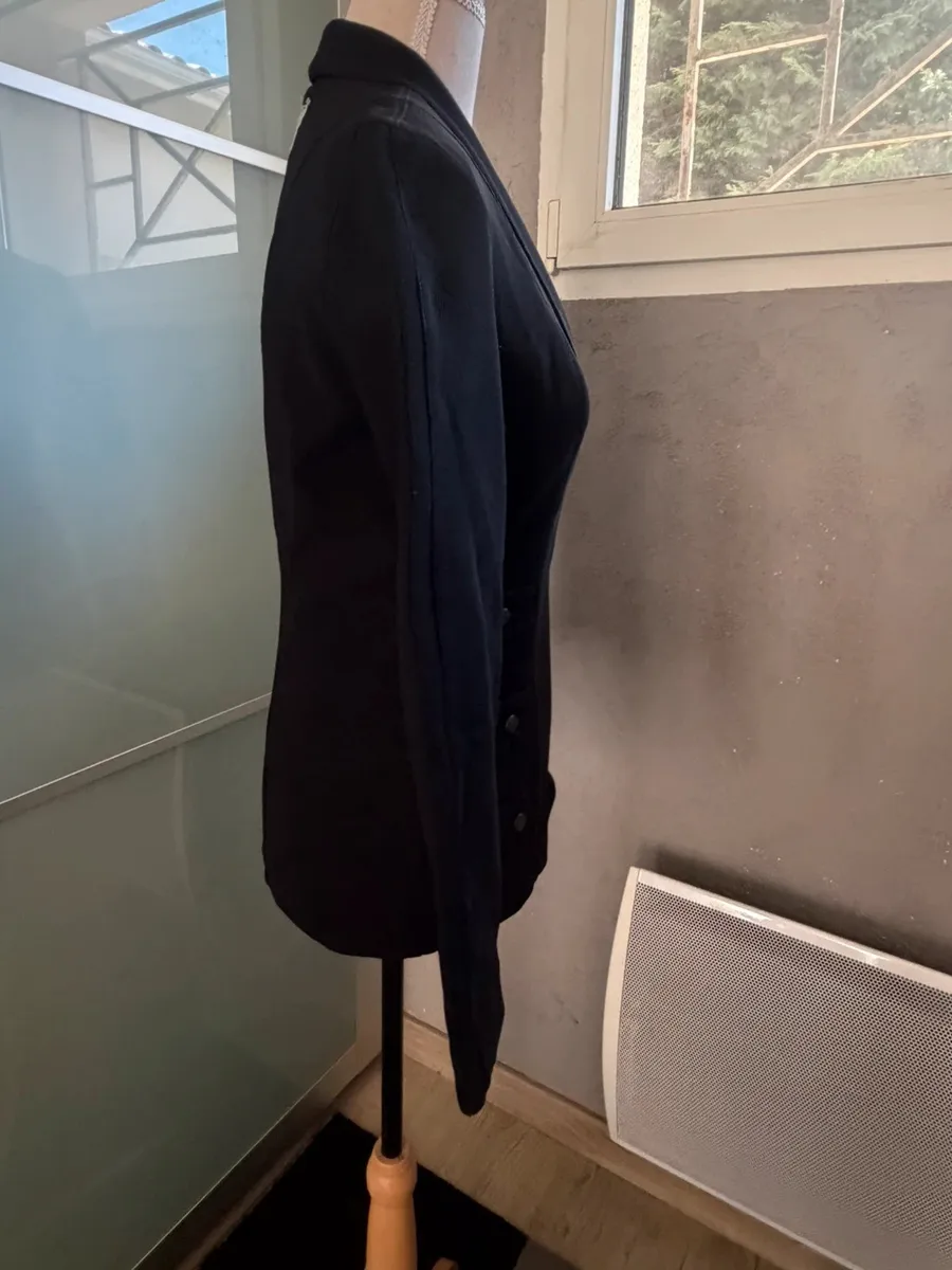 ✨ Une pièce vintage d'exception au style couture et affirmé ! Superbe veste de tailleur / blazer vintage noir de la marque créateur Tony La Marca France, coupe travaillée et très élégante. ✨ Détails & Coupe : Col châle croisé à l'avant, fermeture par bouton, détails de petits boutons décoratifs structurant le côté de la taille. Tissu côtelé / strié de très belle tenue. 📐 Dimensions & Taille : Largeur aisselle à aisselle : 47 cm (convient à un 38 - M). 🧵 Qualité : Belle confection française vintage, pièce originale et structurée. 2