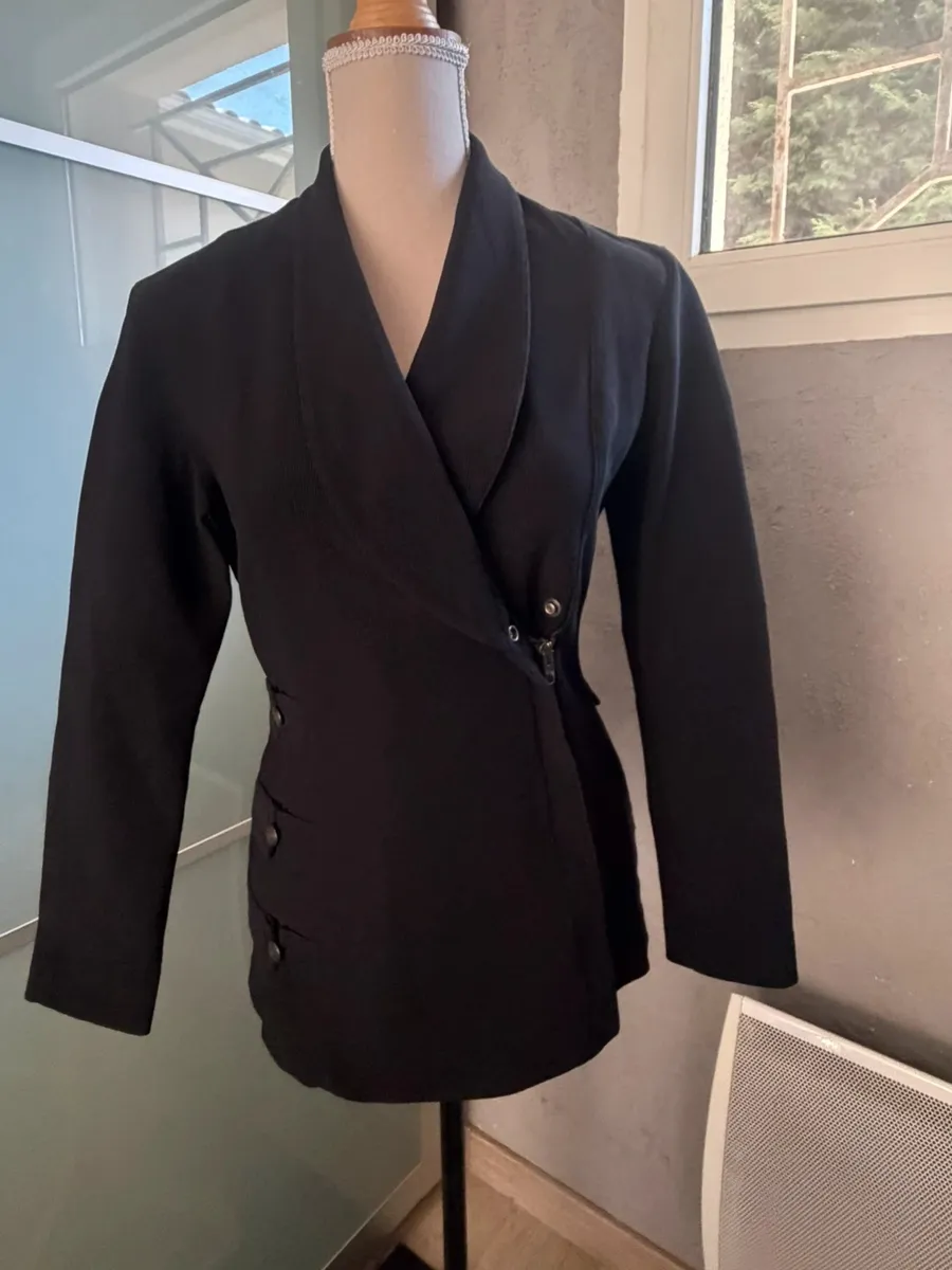 ✨ Une pièce vintage d'exception au style couture et affirmé ! Superbe veste de tailleur / blazer vintage noir de la marque créateur Tony La Marca France, coupe travaillée et très élégante. ✨ Détails & Coupe : Col châle croisé à l'avant, fermeture par bouton, détails de petits boutons décoratifs structurant le côté de la taille. Tissu côtelé / strié de très belle tenue. 📐 Dimensions & Taille : Largeur aisselle à aisselle : 47 cm (convient à un 38 - M). 🧵 Qualité : Belle confection française vintage, pièce originale et structurée. 7
