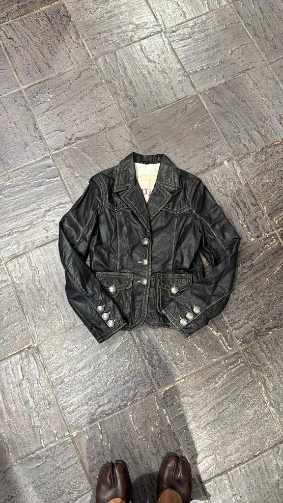 Black leather jacket with decorative silver buttons and contrasting topstitching, featuring two front flap pockets. 4