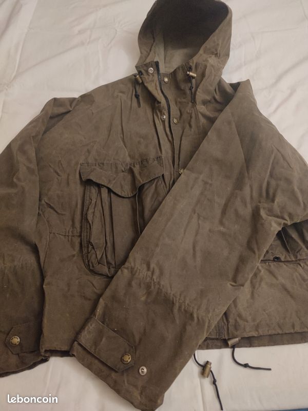 Blouson ou veste courte huilé de la marque FILSON A Genuine C.C. FILSON CO. SEATTLE.
Avec deux poches à l'extérieur et deux poches protège mains, une poche à l'intérieur.
Le bout des manches est tricoté et doublé. Capuche avec lacet de serrage. En parfait état.
C'est une taille L. 5