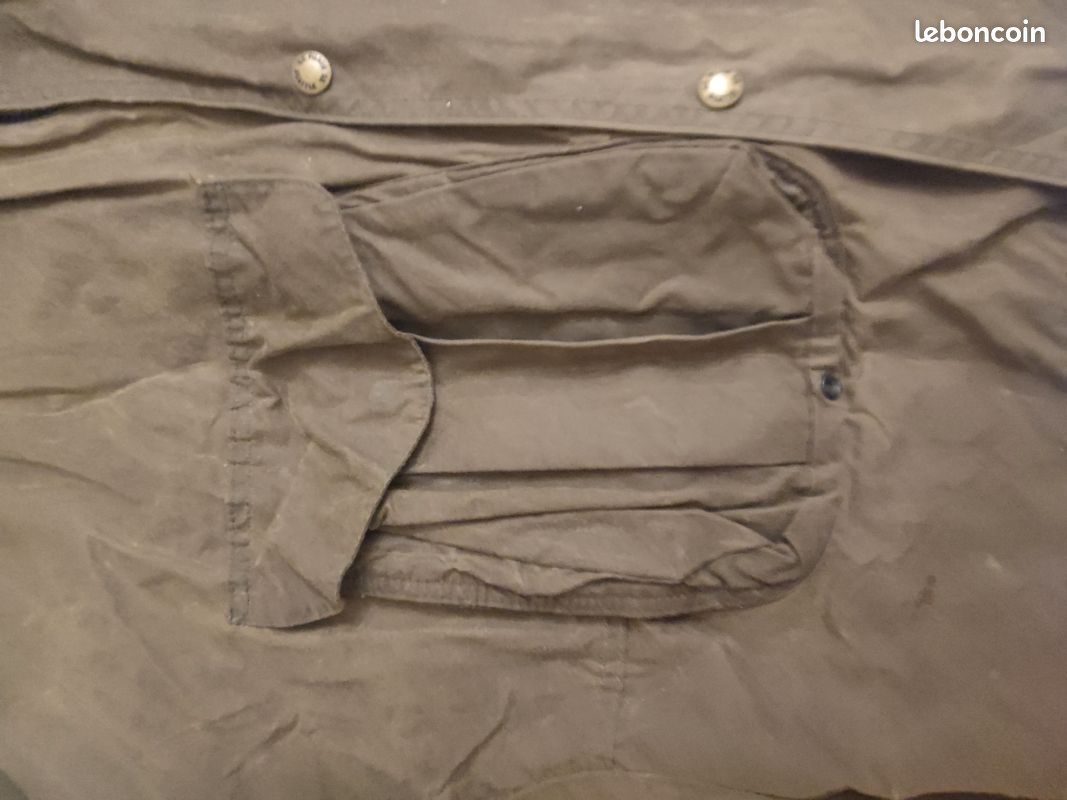 Blouson ou veste courte huilé de la marque FILSON A Genuine C.C. FILSON CO. SEATTLE.
Avec deux poches à l'extérieur et deux poches protège mains, une poche à l'intérieur.
Le bout des manches est tricoté et doublé. Capuche avec lacet de serrage. En parfait état.
C'est une taille L. 9