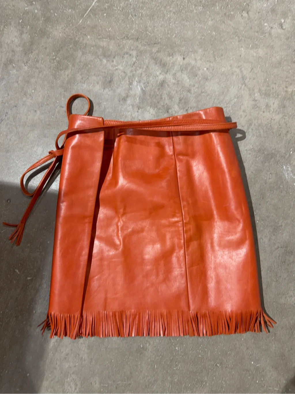 Mini-jupe portefeuille en cuir orange avec franges à l'ourlet.