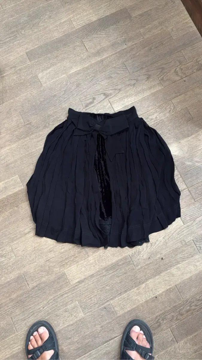 Jupe courte plissée noire Cheap and Chic by Moschino avec un nœud, une doublure en velours et des détails en dentelle.