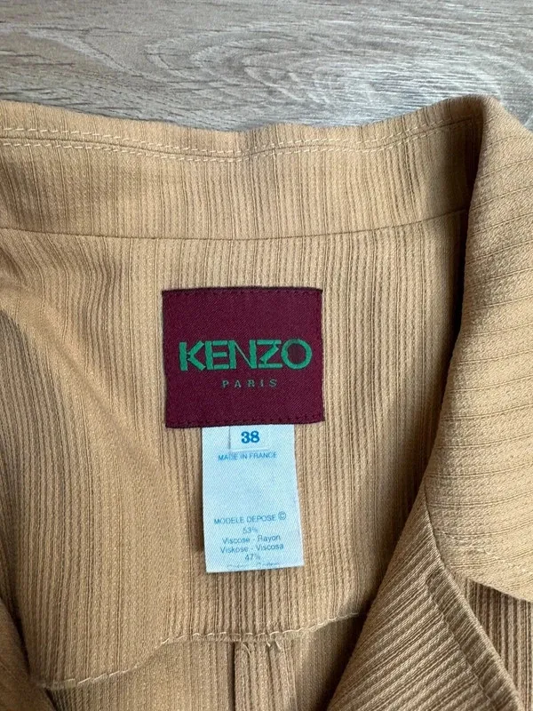 Superbe manteau fin / manteau-robe vintage de la maison Kenzo Paris. Coupe très élégante à la taille, tissu texturé à rayures verticales ton sur ton, col à revers et fermeture par trois gros boutons. Deux grandes poches plaquées sur le devant. Fabrication française de très belle qualité. Matière : 53% Viscose / Rayon, 47% [seconde matière masquée sur l'étiquette, probablement laine ou coton 2
