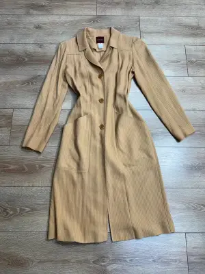 Superbe manteau fin / manteau-robe vintage de la maison Kenzo Paris. Coupe très élégante à la taille, tissu texturé à rayures verticales ton sur ton, col à revers et fermeture par trois gros boutons. Deux grandes poches plaquées sur le devant. Fabrication française de très belle qualité.  Matière : 53% Viscose / Rayon, 47% [seconde matière masquée sur l'étiquette, probablement laine ou coton