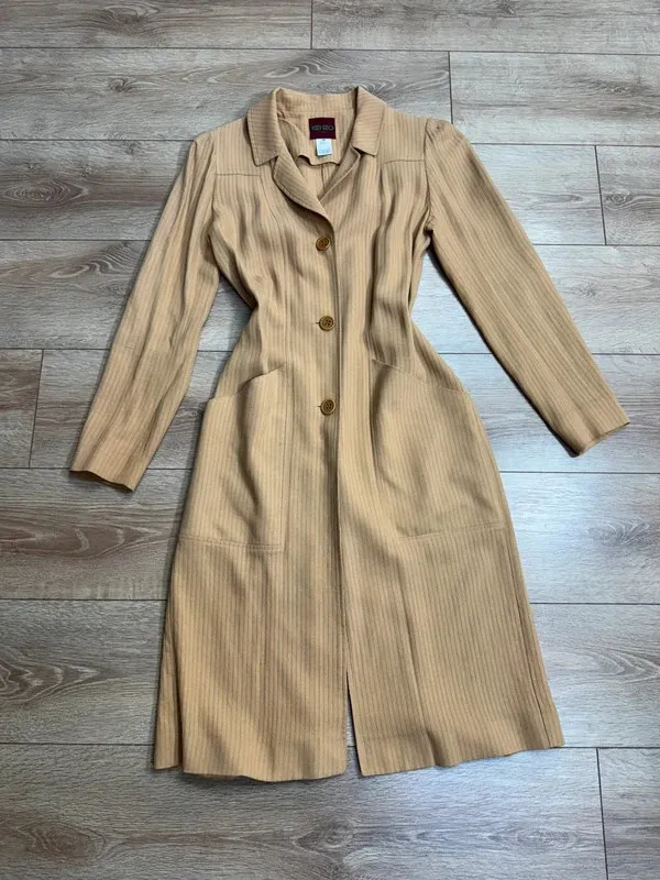 Superbe manteau fin / manteau-robe vintage de la maison Kenzo Paris. Coupe très élégante à la taille, tissu texturé à rayures verticales ton sur ton, col à revers et fermeture par trois gros boutons. Deux grandes poches plaquées sur le devant. Fabrication française de très belle qualité. Matière : 53% Viscose / Rayon, 47% [seconde matière masquée sur l'étiquette, probablement laine ou coton