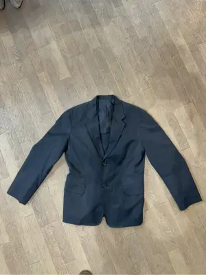 Blazer noir en coton avec fermeture à deux boutons et détail de cordon de serrage à l'arrière.