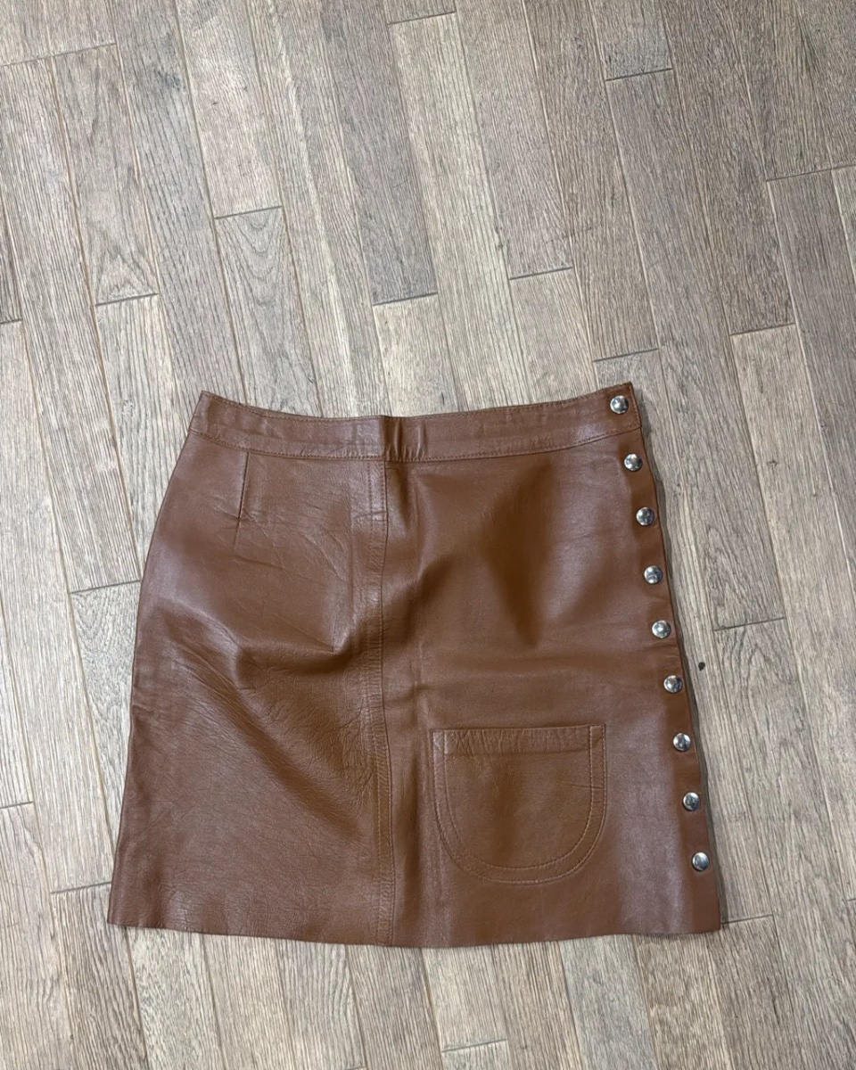 Mini-jupe en cuir marron avec une poche plaquée et des boutons décoratifs sur le côté.